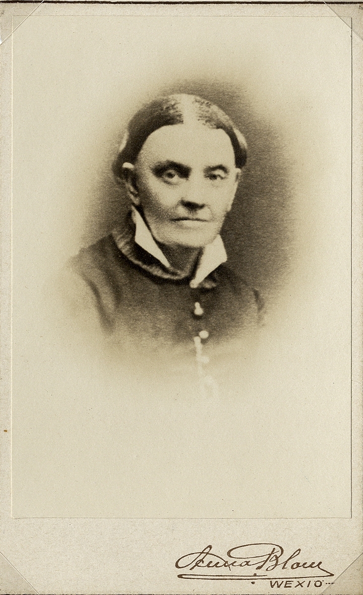 Foto av en äldre kvinna i mörk klänning med vit krage. 
Bröstbild, halvprofil. Ateljéfoto.

Kopia av äldre foto från 1880-talet.