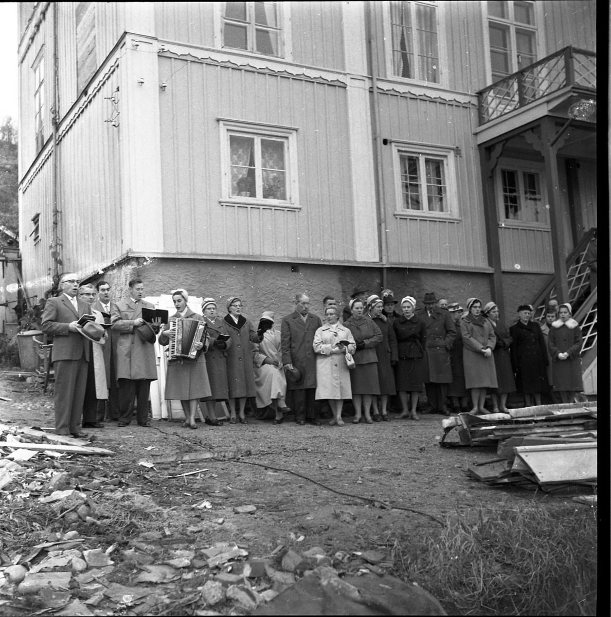 En grupp män och kvinnor på baksidan av Brahegatan 75a (Hjertströmska gården) står och sjunger till ackompanjemang av en kvinna som spelar dragspel. Pastor Robert Svensson står till vänster. Trea från vänster är möjligen Erik Olofsson.