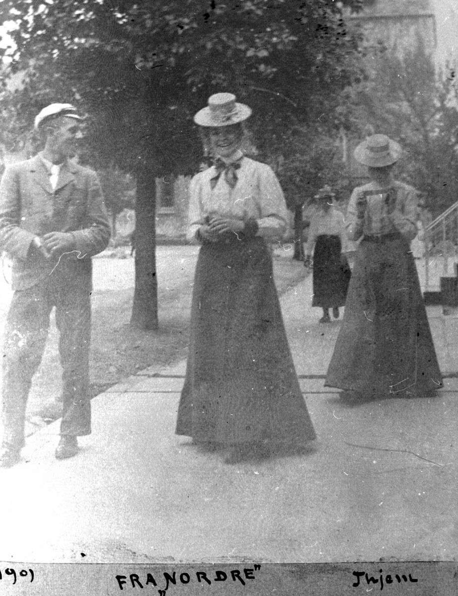 Mann og tre kvinner promenerer på fortau ved park.