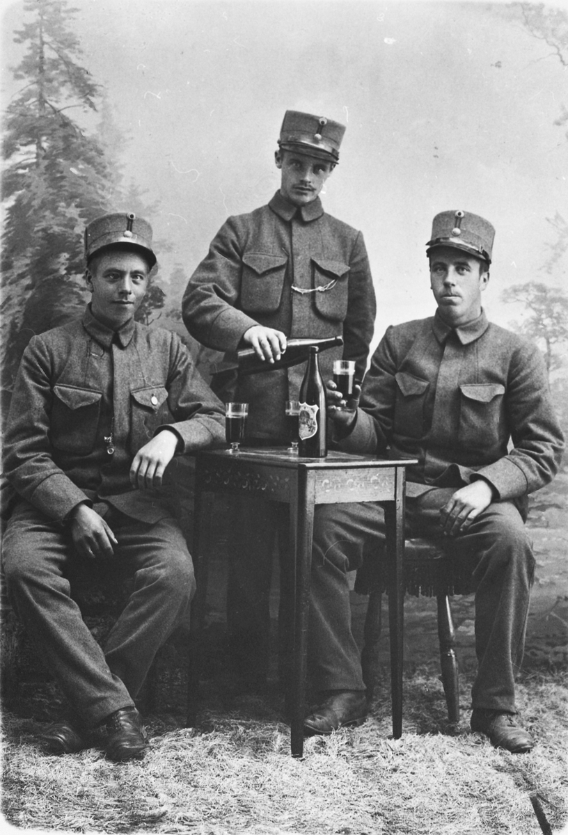 Portrett av tre unge menn i uniform som tar seg en øl