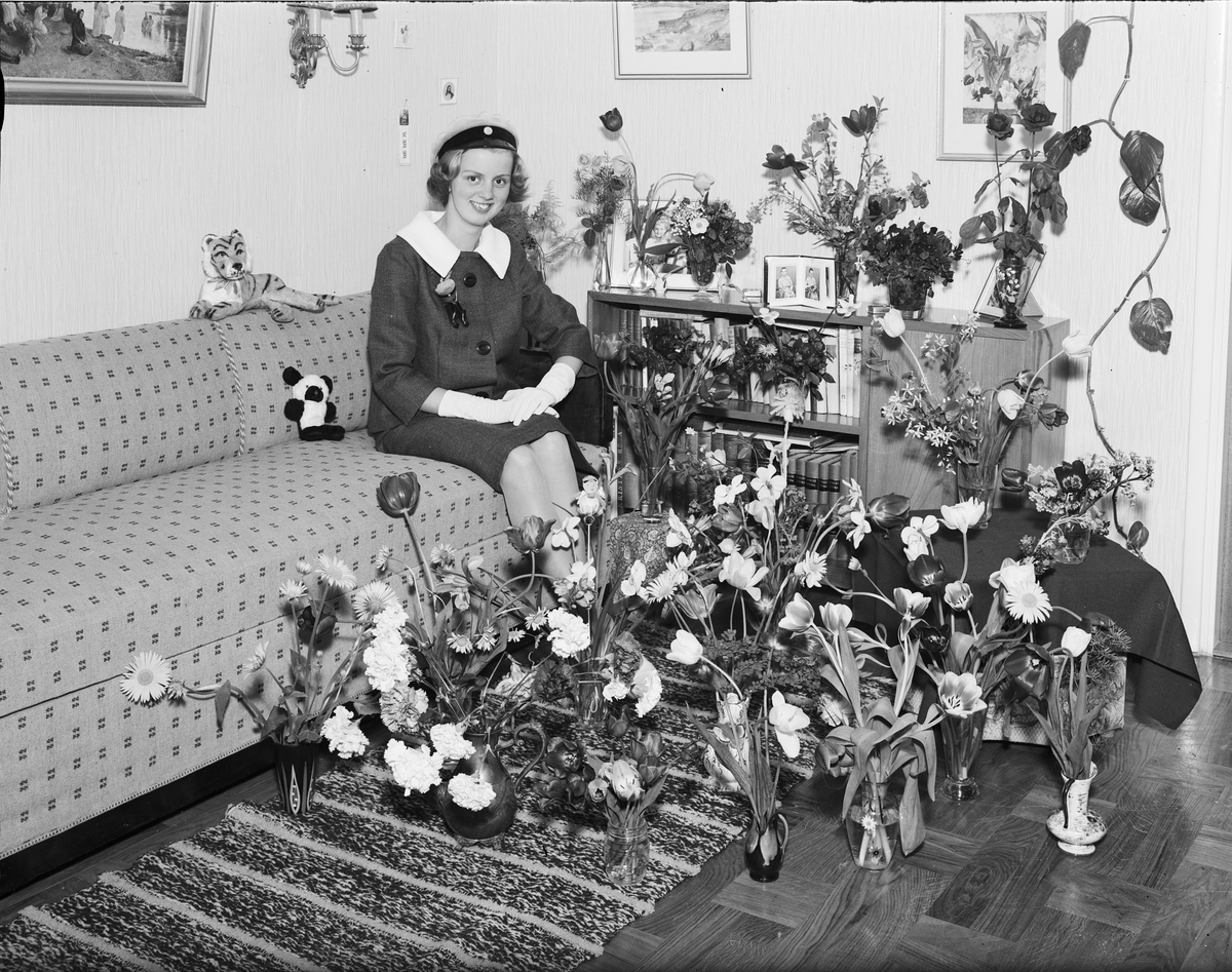 Ung kvinna i hemmiljö omgiven av blommor, Östhammar, Uppland