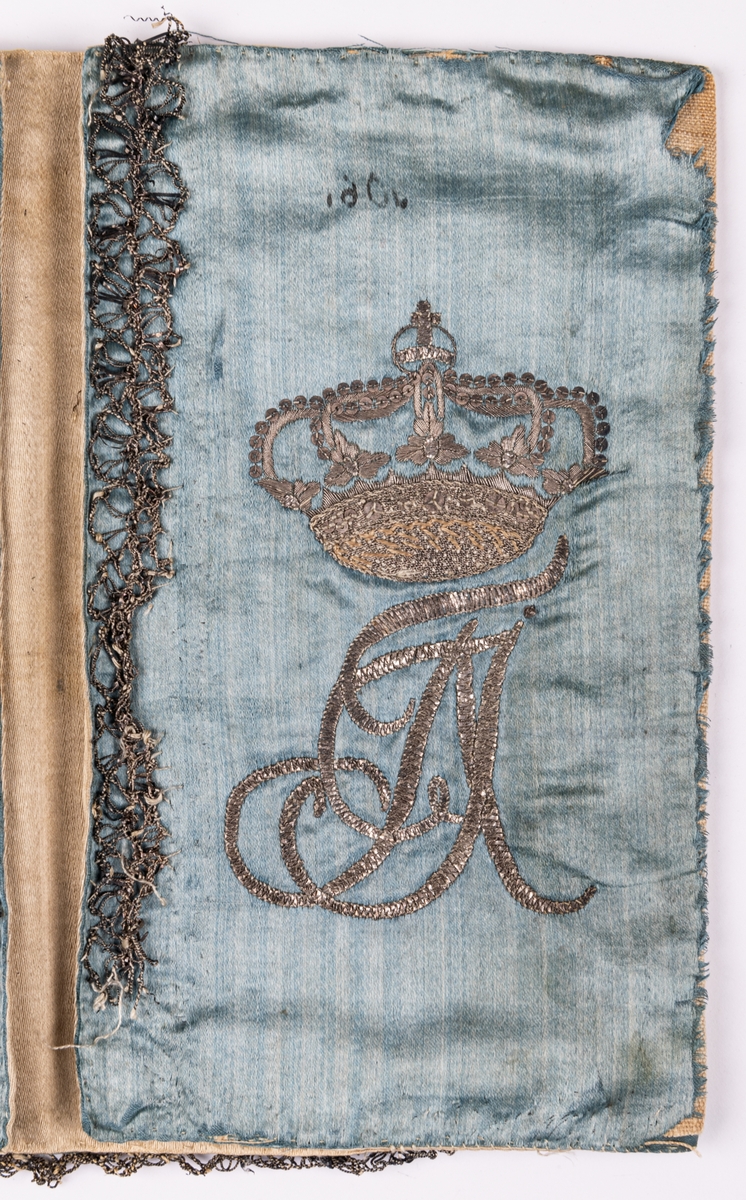 Plånbok av ljusblått siden med silvertrådsbroderi. Insidan "A S F" i monogram under kunglig krona samt en stork. På yttersidorna rokokomässig ram med växtslingor. Kantbårder av silvertråd.