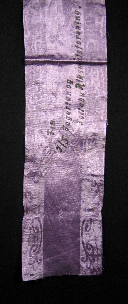 Begravelsessløyfe i lilla mønstret silke med svart tekst.