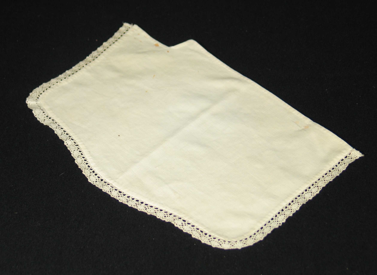 Hvit serviett i bomull kantet med blonde på tre sider. Den er sydd etter formen på hylla.