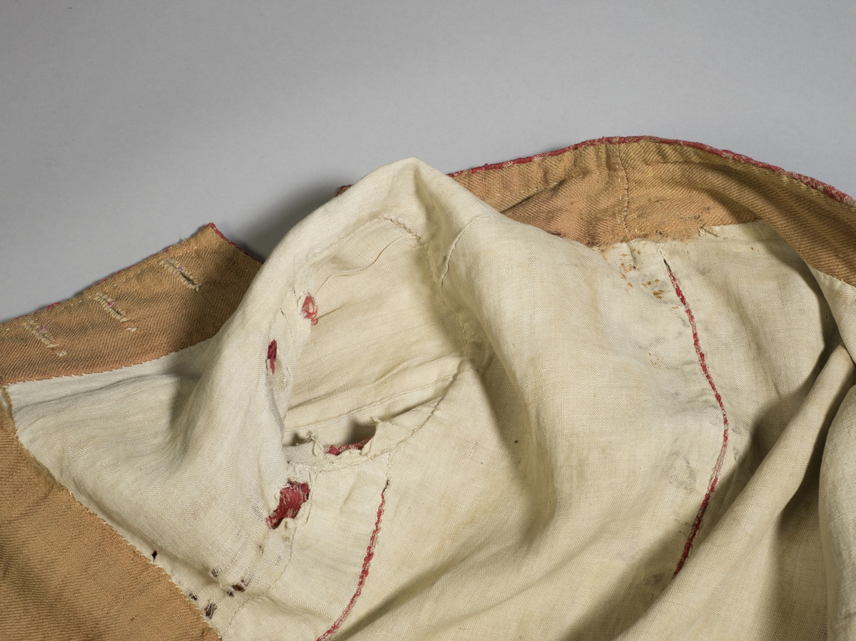 Håndsydd vest av ulldamask, fôret med to typer linstoff. Ryggsømmene er sydd med spilesøm. Vesten har ståkrage, dobbel knapphullrad (18) , trekte knapper (to ulike stoff) (16) - to mangler. Det vil si ni knapphull  og knapper på hvert forstykke. Knapphullene er sydd med lintråd.
To sidelommer. Knapp og knapphull nederst på ermene.