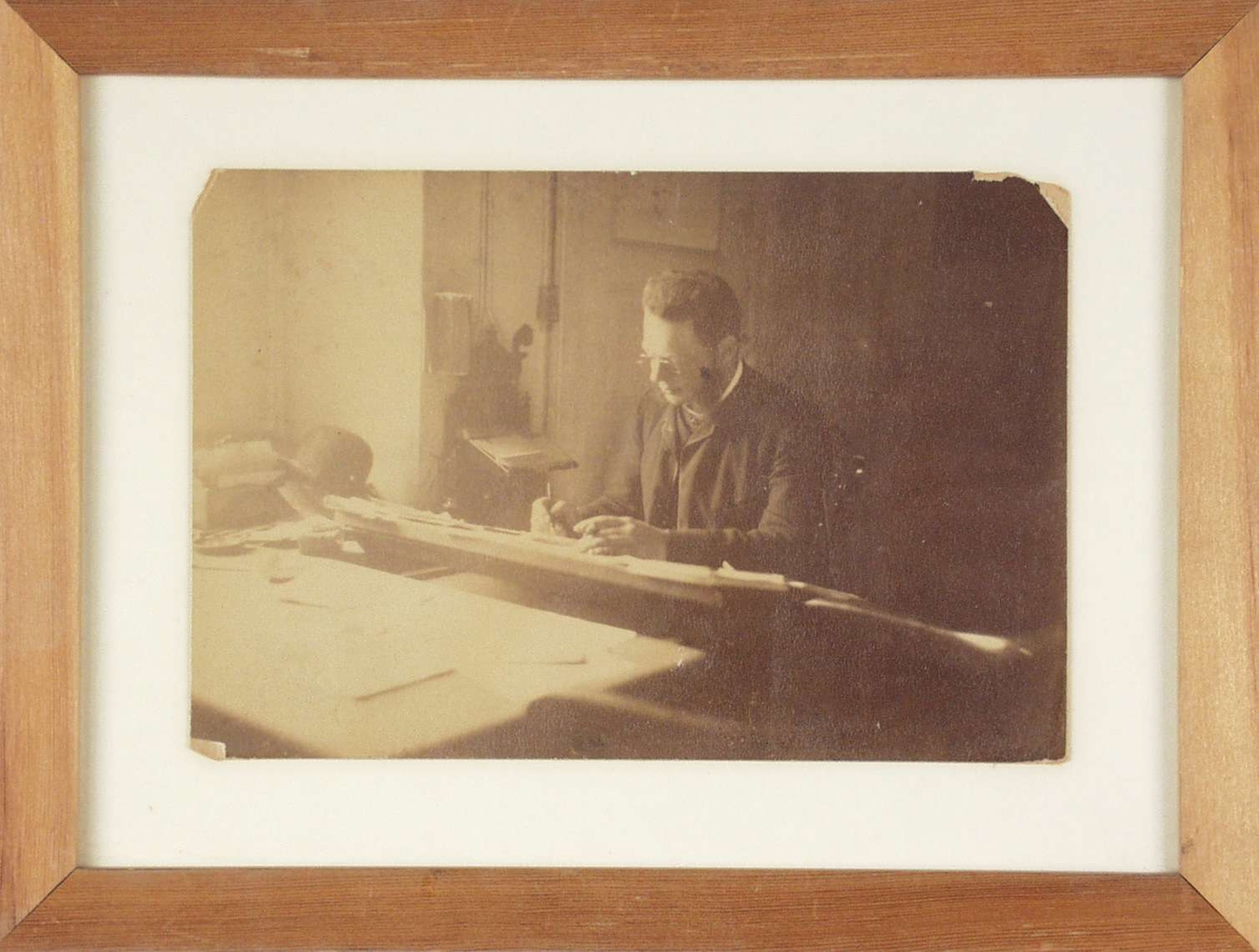 Boktrykker John Grieg som sitter å arbeider ved et bord.