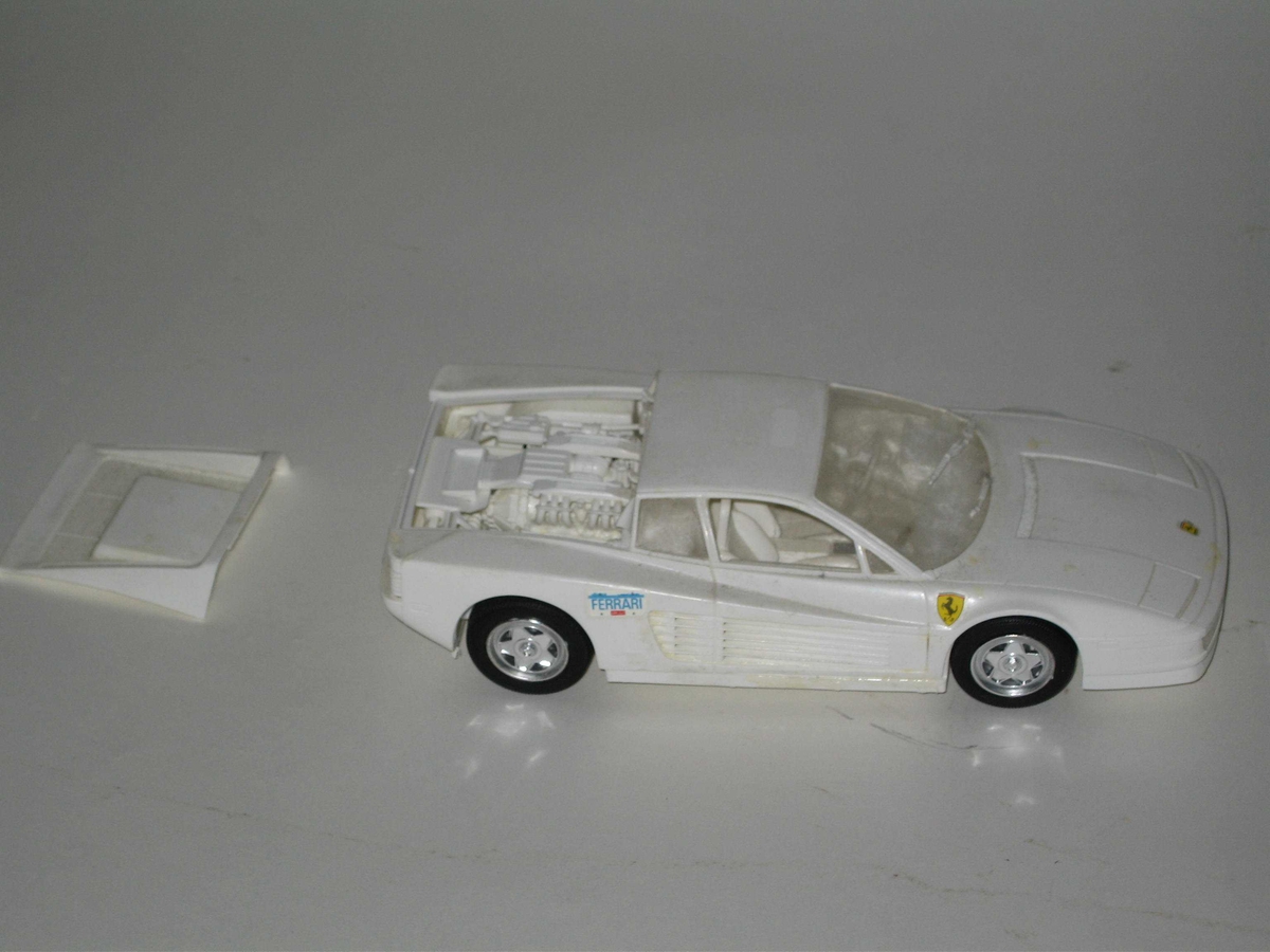 Byggesettmodell av Ferrari Testarossa. Hvitt karosseri, klarplast frontrute og bakre sideruter og frontlykter og svarte dekk med krom felger. Bilen har hekkmotor, og panseret kan tas av.