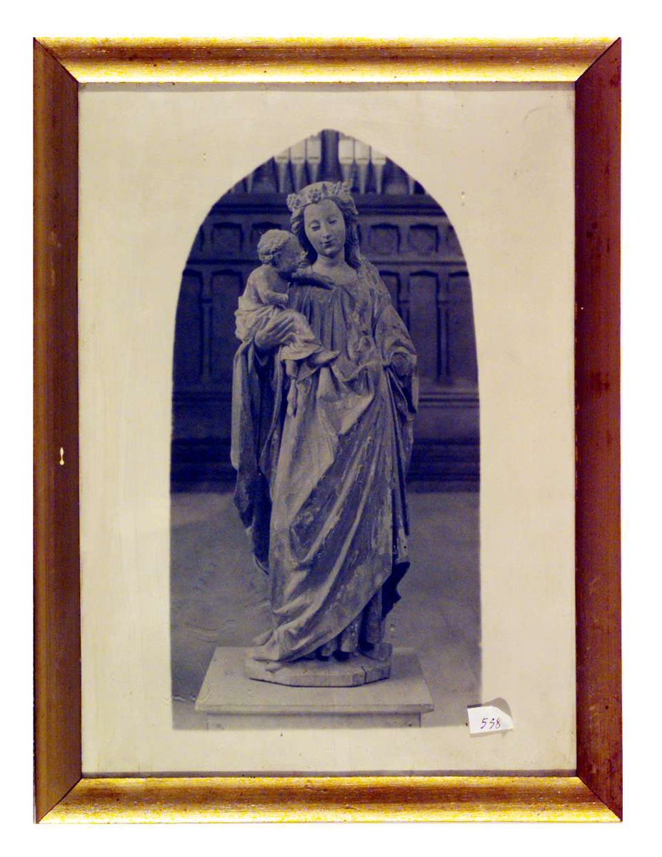 Bildet er en sort/hvit gjengivelse av en malt treskulptur. Skulpturen fremstiller en stående Madonna med Jesusbarnet på armen. 