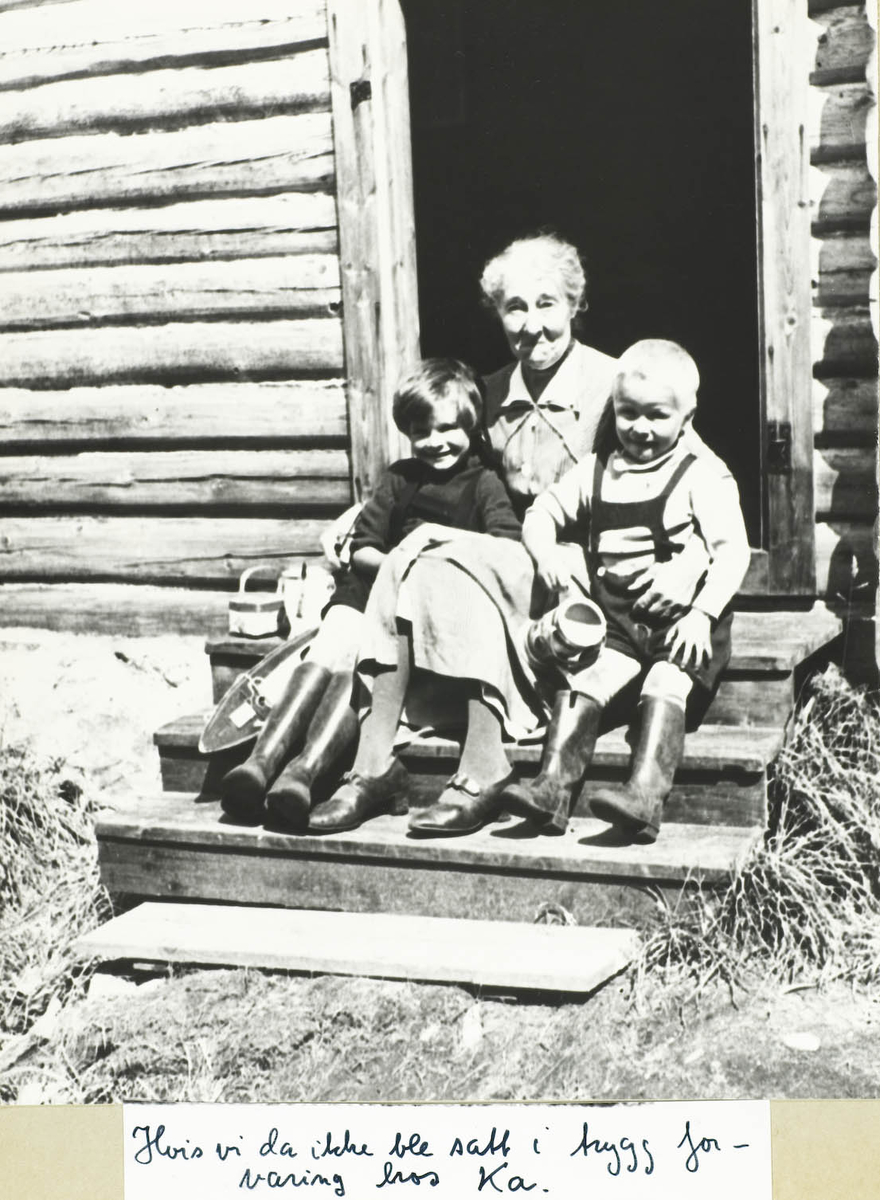 Tre personer, en dame og to barn sittende på en trapp ca 1940