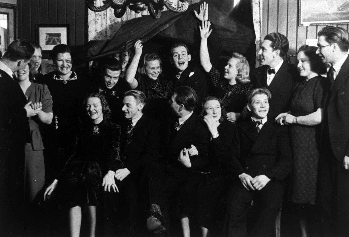 Fest med "nedfall" på Skogvold 1943.
(Det er blendingsgardinen som faller ned) Festkledd forsamling oppstilt for fotografering. De i bakre rekke løfter gardinen over hodet.