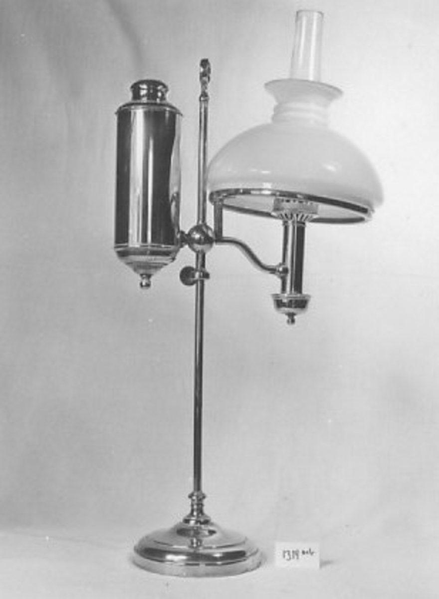A: Lampe;  B: Kuppel: A: sirkelformet, profilert fotplate; stang som ender i ring; på midten kule hvortil festet sylinderformet beholder, på den andre ssiden arm og beholder m. brenner og lampeglass, ring til kuppel

