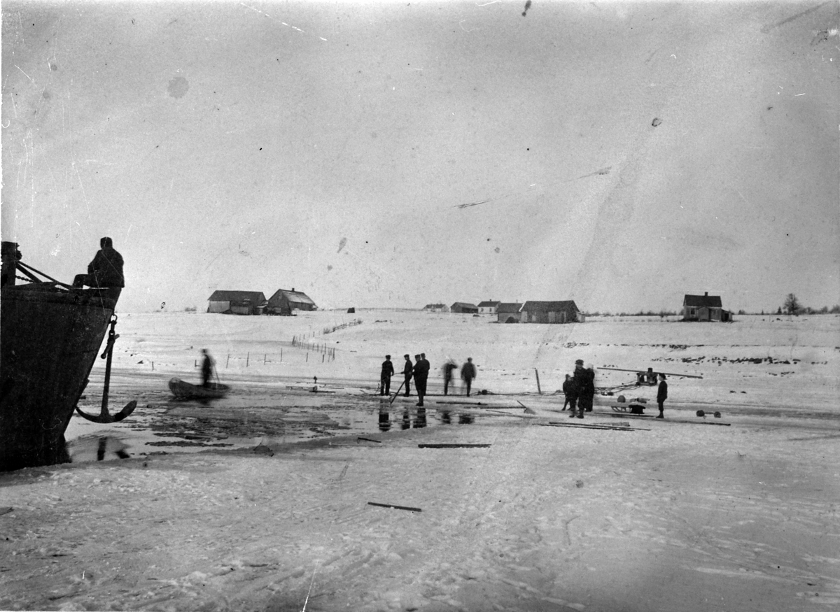Folk sager is på Mjøsa. Baugen på Mjøsbåt, I bakgrunnen er småbruk og husmannsplasser. Ca. 1910. Ukjent sted.