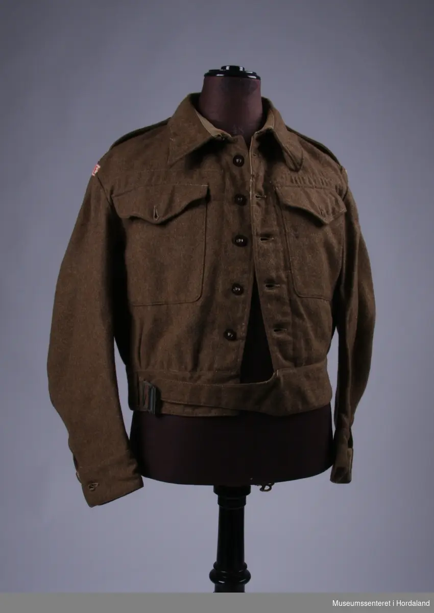 ...(20) Leeds 1943, 56003. Uniform består av 1 jakker, 1 skjorte, 1 bukse, 1 hue, 1 belte, 1 par gamasjer, 1 slips og 1 epålett. Jakka har påsydd Bjørn West stempel. På epåletten er det trykt på et norsk flagg og sydd på 3 raude striper.