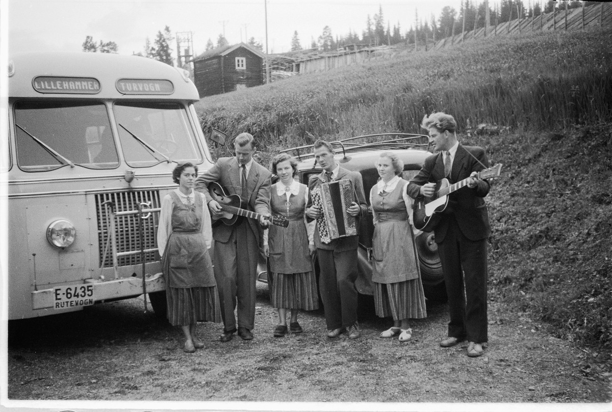 Tre menn spiller gitar og trekkspill, mens tre kvinner lytter ved en buss med skilt Lillehammer turvogn. T. h. Ulf Sæhli på gitar. Volvo buss E-6435, Lillehammer Ringsaker Bilruter.