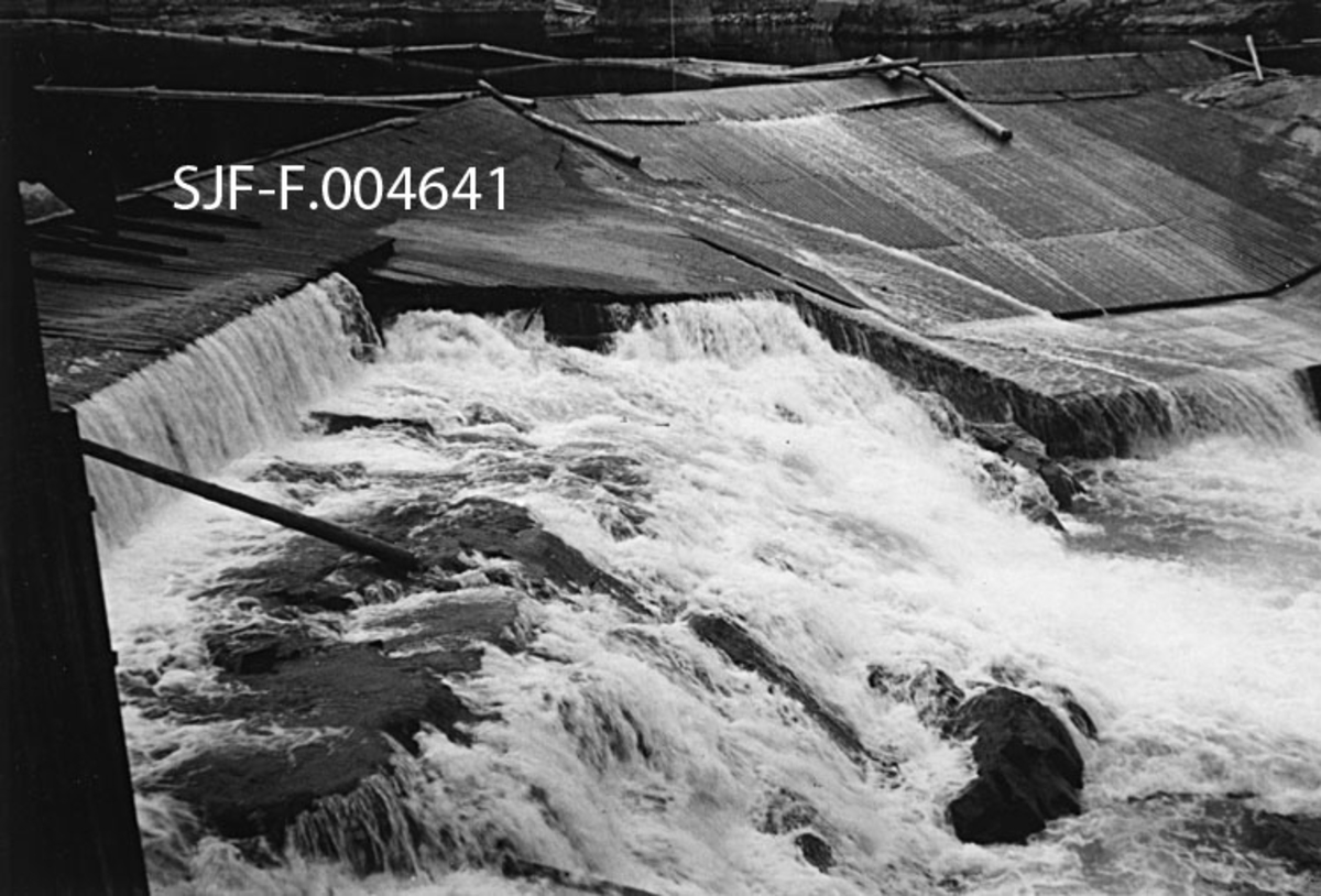 Geithusfossen på Modum i Buskerud, slik den så ut 21. oktober 1945, på et tidspunkt da vannføringa i Drammenselva var ekstremt lav (33 kubikkmeter per sekund).  Fotografiet er tatt fra østsida av fossen (akkurat her renner elva nordover) med sjølve fallet som hovedmotiv.  På grunn av den beskjedne vannføringa ser vi tydelig hvordan det var bygd en terskel like ovenfor fallet.  Vi ser også hvordan den midtre delen av fosseløpet var golvlagt, med sikte på at tømmer som skulle videre nedover i fossen ikke skulle sette seg fast så lett.  Øverst på bildeflata ser vi også hvordan elva var lenselagt med sikte på at fløtingstømmeret skulle ledes mot denne golvlagte delen av fossefallet. 