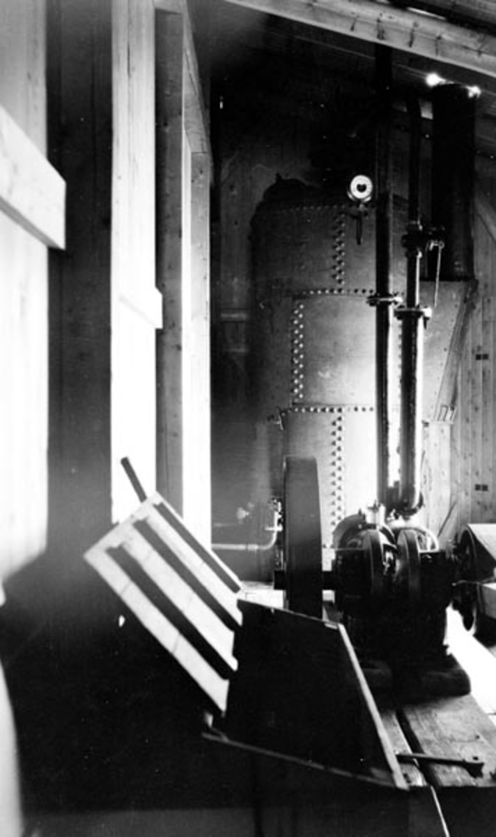 Fra maskinrommet til det første soppeapparatet som ble bygd ved Lillehammer lense i 1909, for å bunte tømmer som skulle slepes langsetter Mjøsa til Minnesund og Vorma.  Fotografiet er tatt inne i et bordkledd bindingsverksrom med enkelt panel og pulttak.  Ved endeveggen står en sylindrisk dampkjele av sammenklinkete jernplater med et manometer på toppen.  På golvet foran står en slags motor med reimskive.  Foran denne står ei trekasse, muligens ei redskapskasse med skrått lokk, som da dette fotografiet ble tatt sto vidåpent.

Da Kristiania Tømmerdirektion i 1903 vedtok å overta administrasjonen av fløtinga på Mjøsa hadde Lillehammer lense lenge hatt lokalt eierskap. Den nevnte beslutningen fikk i første omgang ingen annen konsekvens for lensedriften enn at det fra da av var Tømmerdirektionen som inviterte til anbud på driften av de 8 lenseanleggene som fantes der fløtingsvassdragene rant inn i innsjøen. I 1908 inngikk Kristiania Tømmerdireksjon forpaktningsavtale for Lillehammer lense, og det var denne organisasjonen som moderniserte anlegget. De to første sesongene, i 1909 og 1910, ble soppeapparatene drevet av en dampmaskin. Etter dette inngikk Tømmerdireksjonen avtale med Lillehammer kommunale elektricitetsverk om leveranser av elektrisk energi. Fra da av ble soppinga av tømmer utført med elektromotorer som drivkraft. Dampkjelen på dette fotografiet ble etter dette flyttet til Fetsund lenser, der den ble brukt til å manøvrere soppeapparatene på Lertanglensa.

Onsdag 12. mai 1909 beskrev avisa «Lillehammer Tilskuer» det nye soppeapparatet ved byens lenseanlegg slik:

«Soppemaskinen ved Lændsen er nu paa det nærmeste færdig. Det bestaar av to 64 Meter lange flydende Broer, der holdes sammen av to 12 M. lange Tverbroer. Paa den ene Langside ligger Maskinen. Hele Apparatet ligger paa langs i Strømretningen. Tømmeret kommer drivende ind i den øvre Ende, og føres af Strømmen ned mod to flere Meter dybe Arme, der stikker ned fra den nederste Tverbro. Her hobes det da op, og det slig, at Stokkene blir liggende paa tvers imellem begge Langbroer. Naar hele Rummet er fyldt trækkes en forskyvelig Bro, der ogsaa er forsynet med nedstaaende Arme, nedover af Maskinen, og derved presses Tømmeret sammen i en flere Meter dyb Sop. Der slaaes Staaltraadbaand om, og Soppen er færdig. Armene paa den nederste Tverbro løftes op og Soppen flyder ud. Saa begyndes der paa igjen paa samme Maade.»

Dampmaskinen som drev anlegget fra starten av kunne fyres med ved.