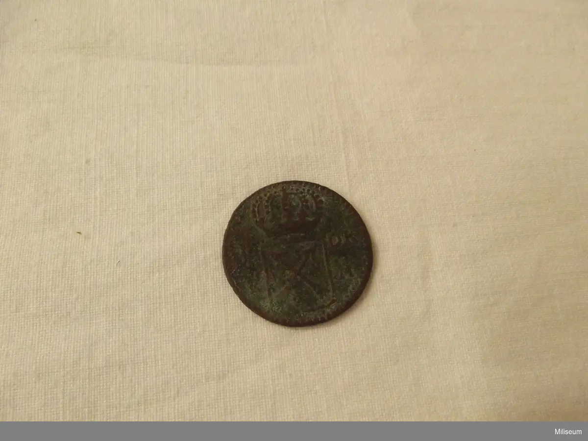 Mynt av koppar, präglat år 1720. 
1 öre i kopparmynt, präglat under drottning Ulrika Eleonoras regeringstid, år 1720. Myntet är upphittat av kn Arthur Haknert på 1970-talet, i nordvästra hörnet av "Slätten"