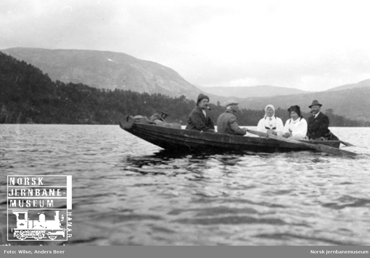 Fem personer, hvorav to kvinner i bunad, i robåt på Store Bjørnevatn i Setesdal