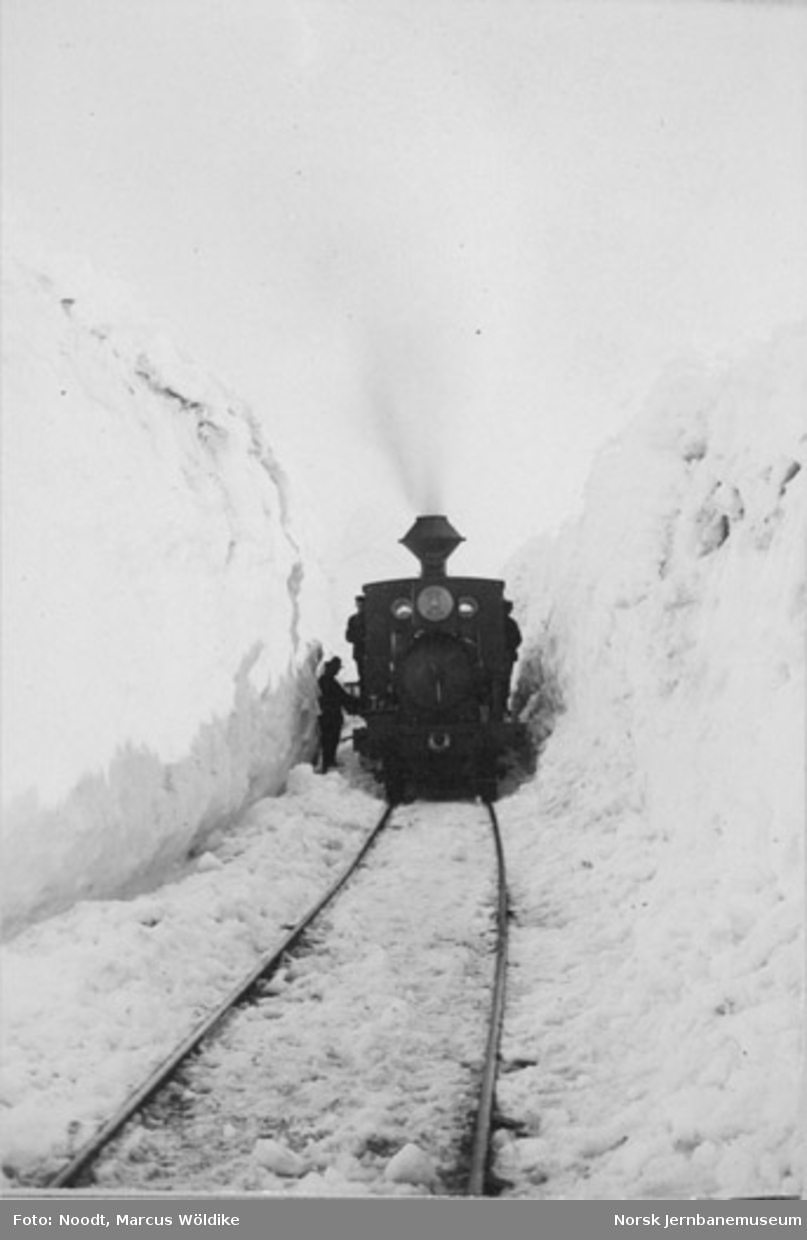 Damplokomotiv type VI mellom høye brøytekanter på Arvedalslinjen (Kongens Grubes bane) pæl 600, sett i retning Rugldalen