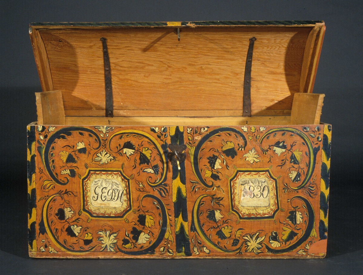 Kiste med svakt buet lokk og rosemalt dekor. Kisten har hatt tilhørende sokkel.