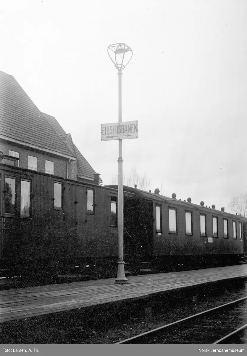 Plattformen på Tønsberg stasjon med skilt "Eidsfosbanen" og tog i spor 1