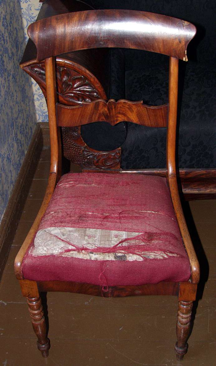 Stol med stoppet sete med rødt ulltrekk. De to fremre beina er dreid og de to bakre lett buede. Ryggen består av en øvre buet del og en midtdel som er figurskåret.