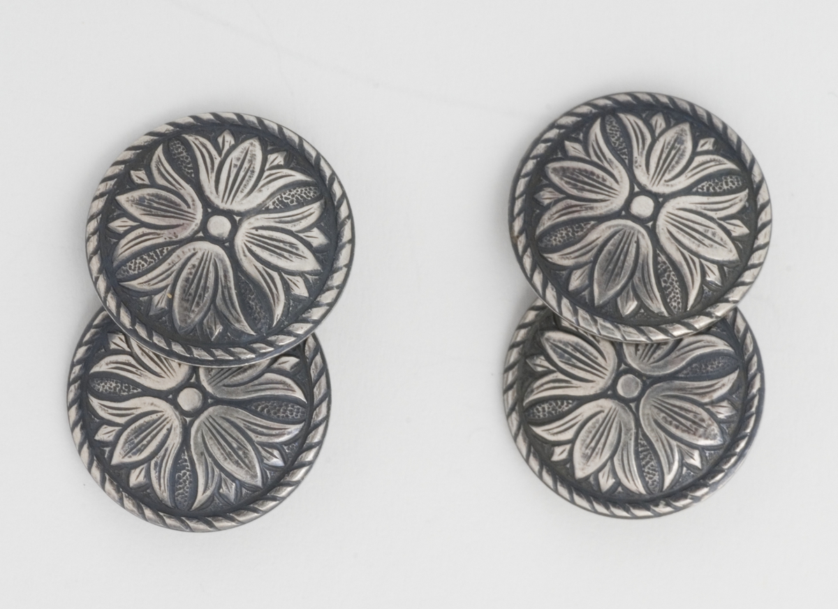 Et par mansjettknapper med blomstermotiv. Hver knapp består av to like knapper er lenket sammen. 