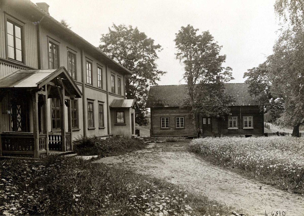 Plogstad, Ullensaker, Øvre Romerike, Akershus. Våningshuset og et mindre hus mot gårdsplassen og blomstereng.