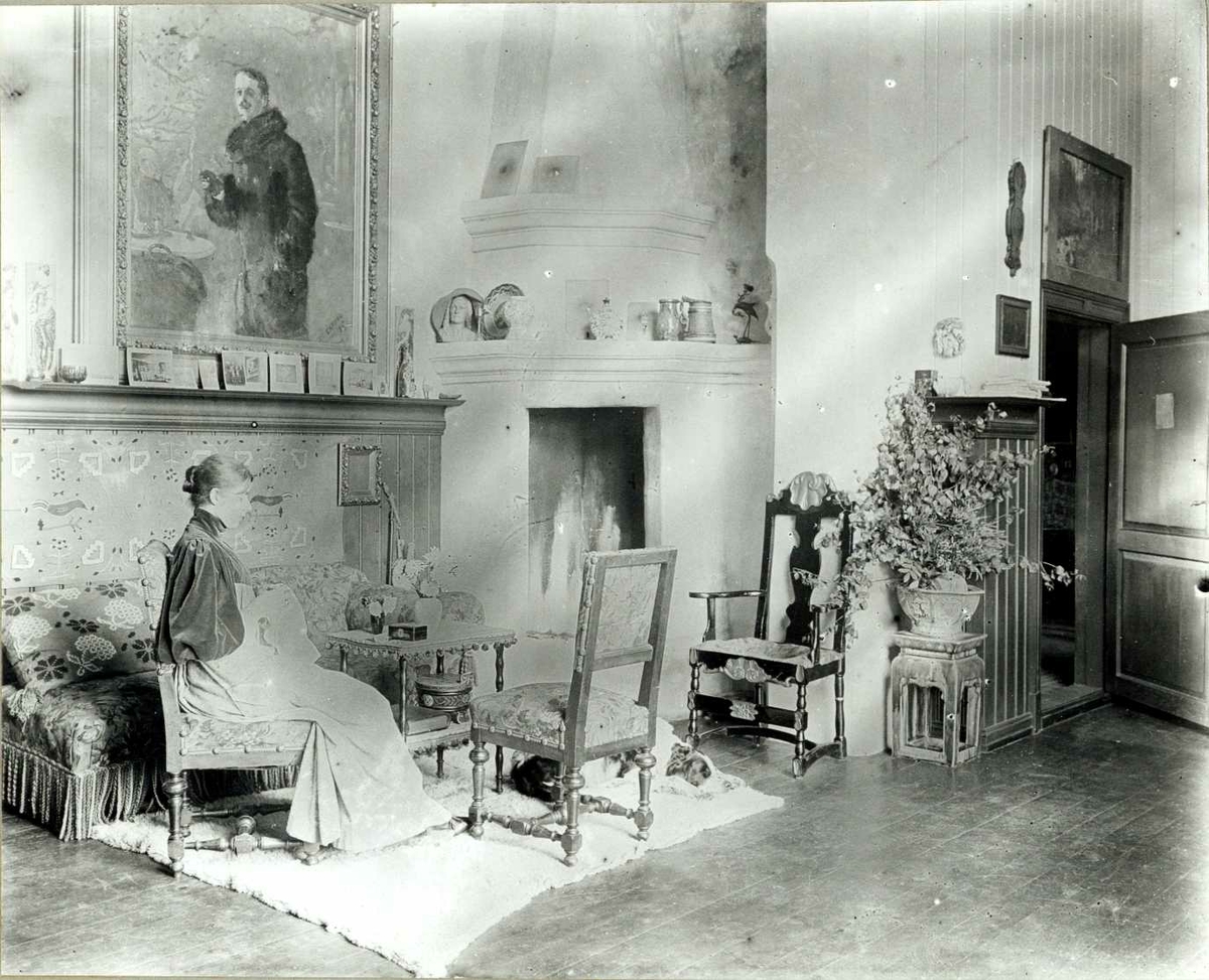 Gerhard Munthes hjem, Stabekk Slott, Bærum, Akershus. Interiør med kvinne sittende under maleri ved peis. Gerhard Munthes hjem i 1890-årene.