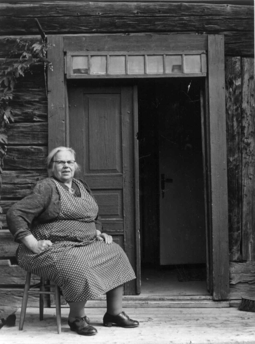 En kvinne sitter ved inngangspartiet til et gammelt hus Vilhelmina, 1956