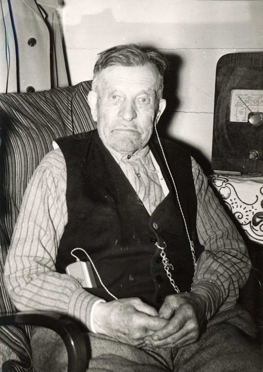 Portrett av Sigurd Olsen, Notodden , sittende i stol ved radio og med høreapparat.