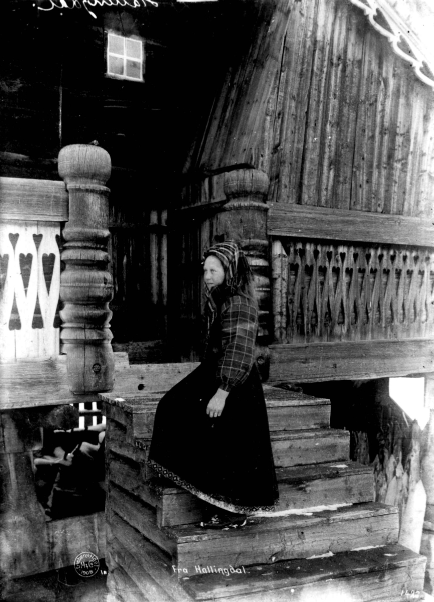 Hallingdrakt. Kvinne på trappa foran et hus.