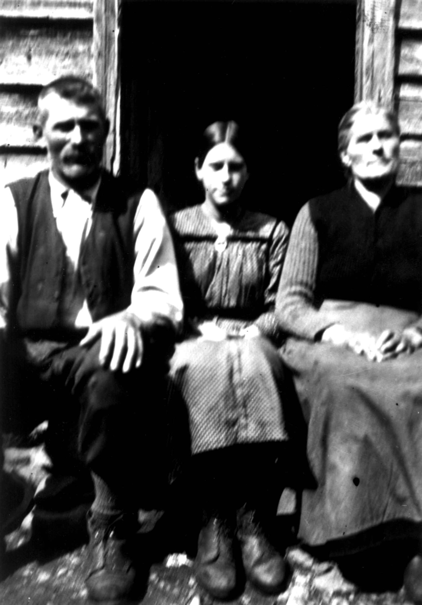 Kvinne- og mannsdrakt, gruppeportrett, Valle, Setesdal, Aust-Agder, antatt 1924. Gruppe sittende foran tømmervegg utendørs. Fra "De Schreinerske samlinger" (skal oppgis).