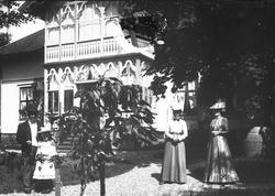 Familieportrett, to kvinner, mann og en pike i hagen foran i