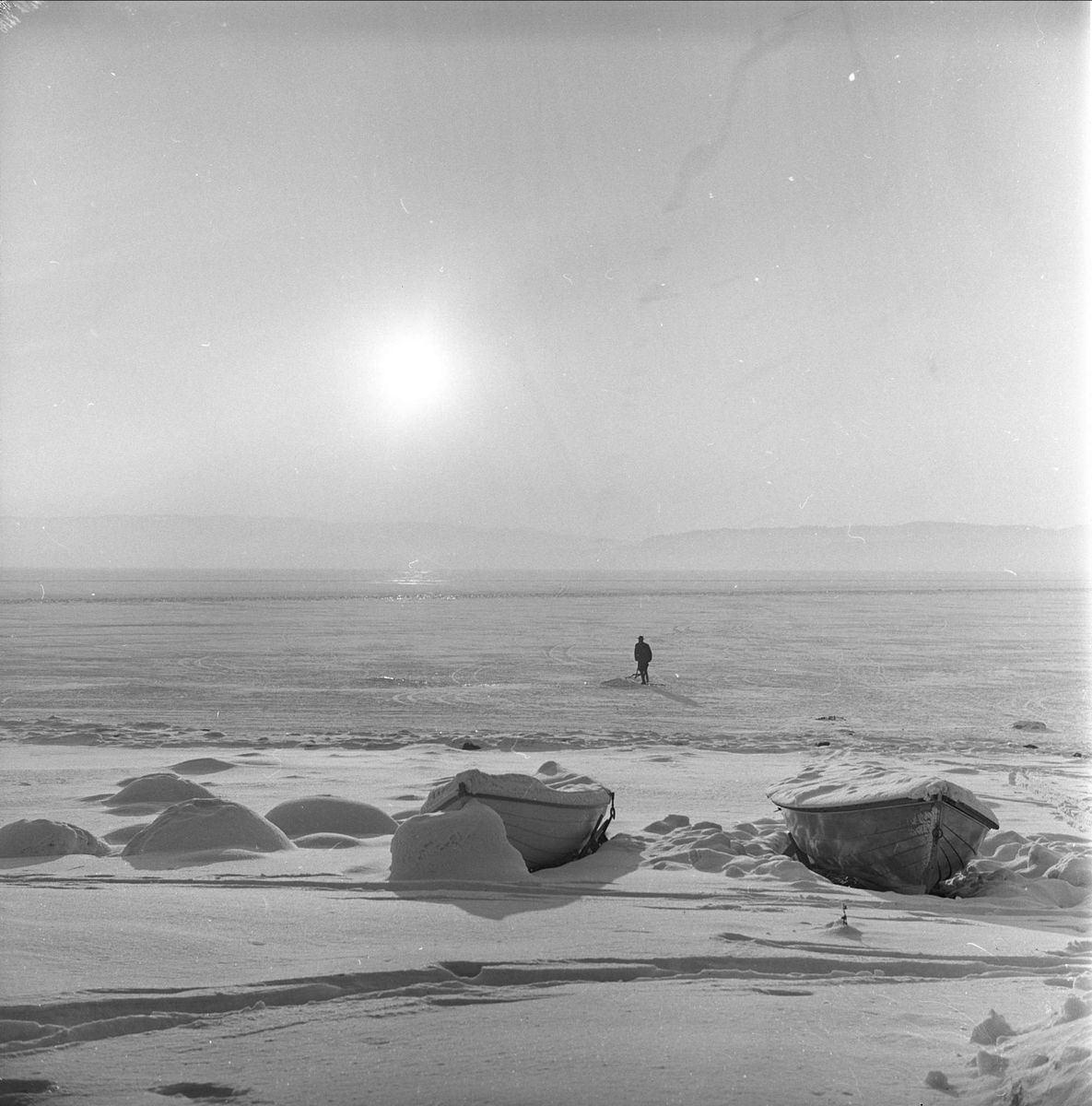 Div. glimt fra Hamar i forbindelse med NM på skøyter, 15.01.1963. Mann på spark, islagt Mjøsa, med båter dekket av snø.