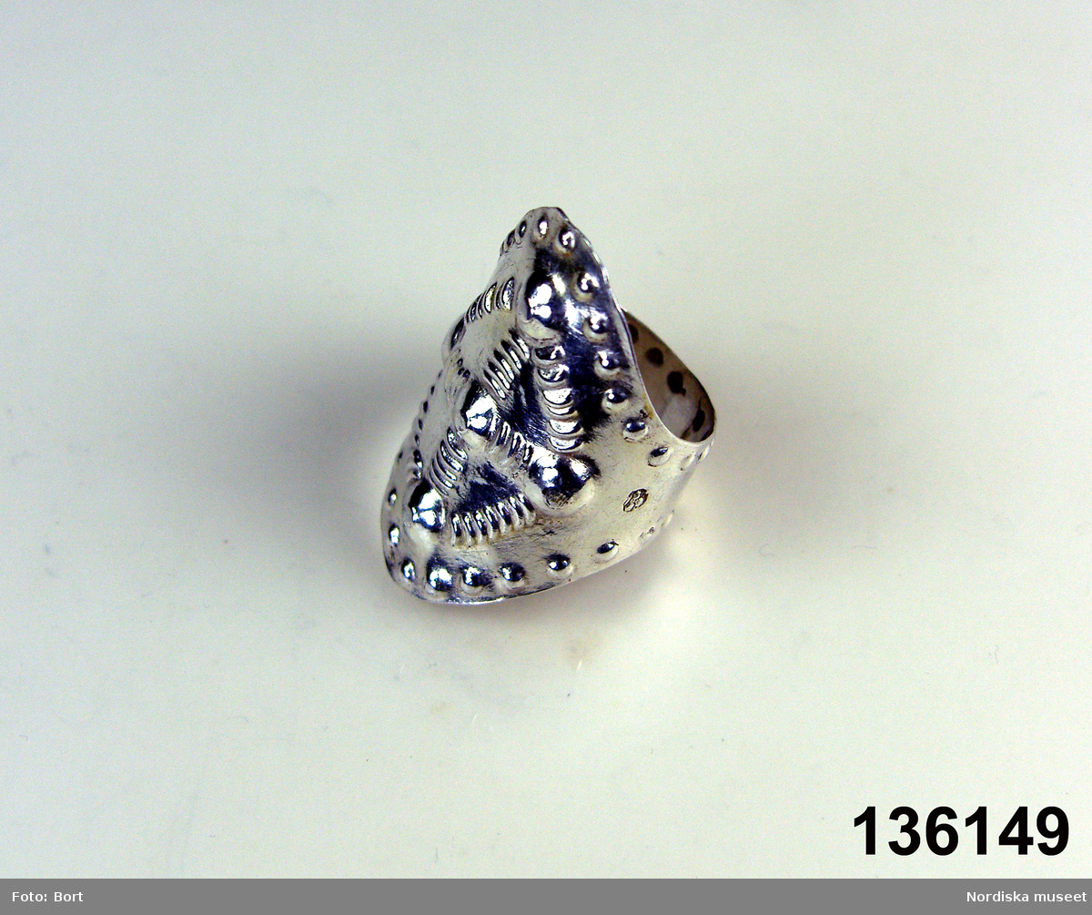 Huvudliggaren:
"Fingerring av silver, med prässad ornering, bred. Stämplad 'L M K / [tre kronor]"