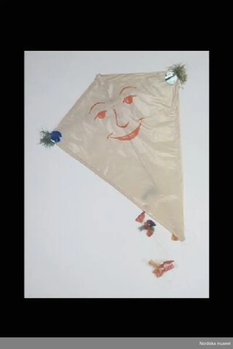 Inventering Sesam 1996-1999:
L  90   B  70 (cm)
Drake, leksak, stomme av trä klädd med vitt papper med motiv av tryckt orange ansikte, gröna pappersremsor och blå runda papperslappar vid två hörn, svans av snöre med rosetter i gult, rött, blått och grönt papper. Påklistrad prislapp: "3.75".
Anna Womack mars 1998