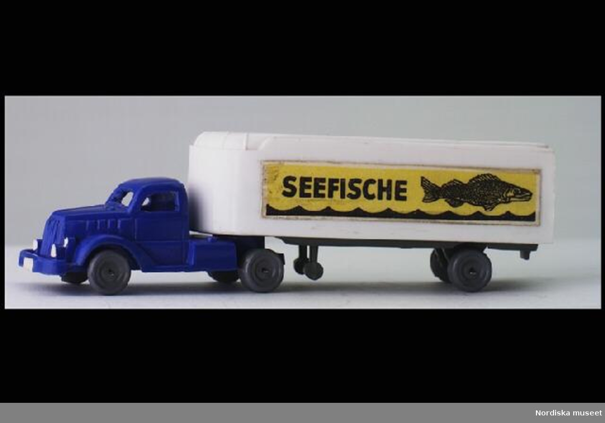 Inventering Sesam 1996-1999:
L 11,7   B 2,8  H 3,5 ( cm)
Dragbil samt släpvagn/trailer. Dragbil i blå plast, ihålig, öppna fönster, grå plasthjul. Släp i vit plast, markerade ej öppningsbara dörrar i bak. Påklistrade dekaler på sidorna med texten: "SEEFISCHE" och en bild av en fisk och böljande vatten. Saknar märkning. Enligt bilaga inköpt 16/4 1952 av givaren för 2,95 hos Eskader, Stockholm. Givaren, samlare av leksaksbilar 1947-1952, se inv nr 263.905 - 264.120.
Bilaga
Helena Carlsson 1996
