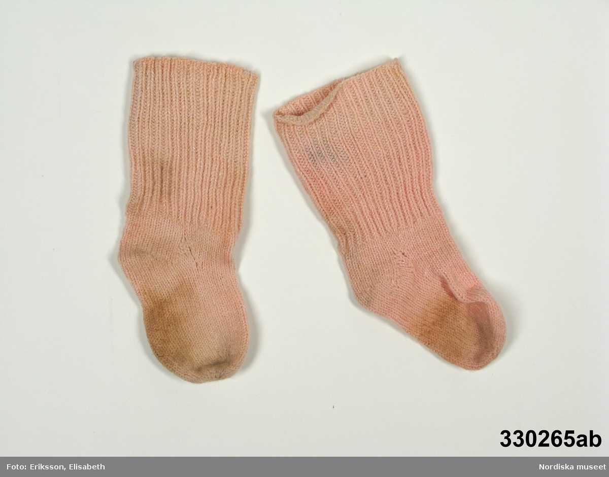 Laxrosa stickade sockor [a-b] för ca 1-2-årig flicka. Foten slätstickad, skaftet ribbstickat och något bredare upptill.
Anm: Ställvis fläckig.
/Zingoalla Rosenqvist 2010-04-08