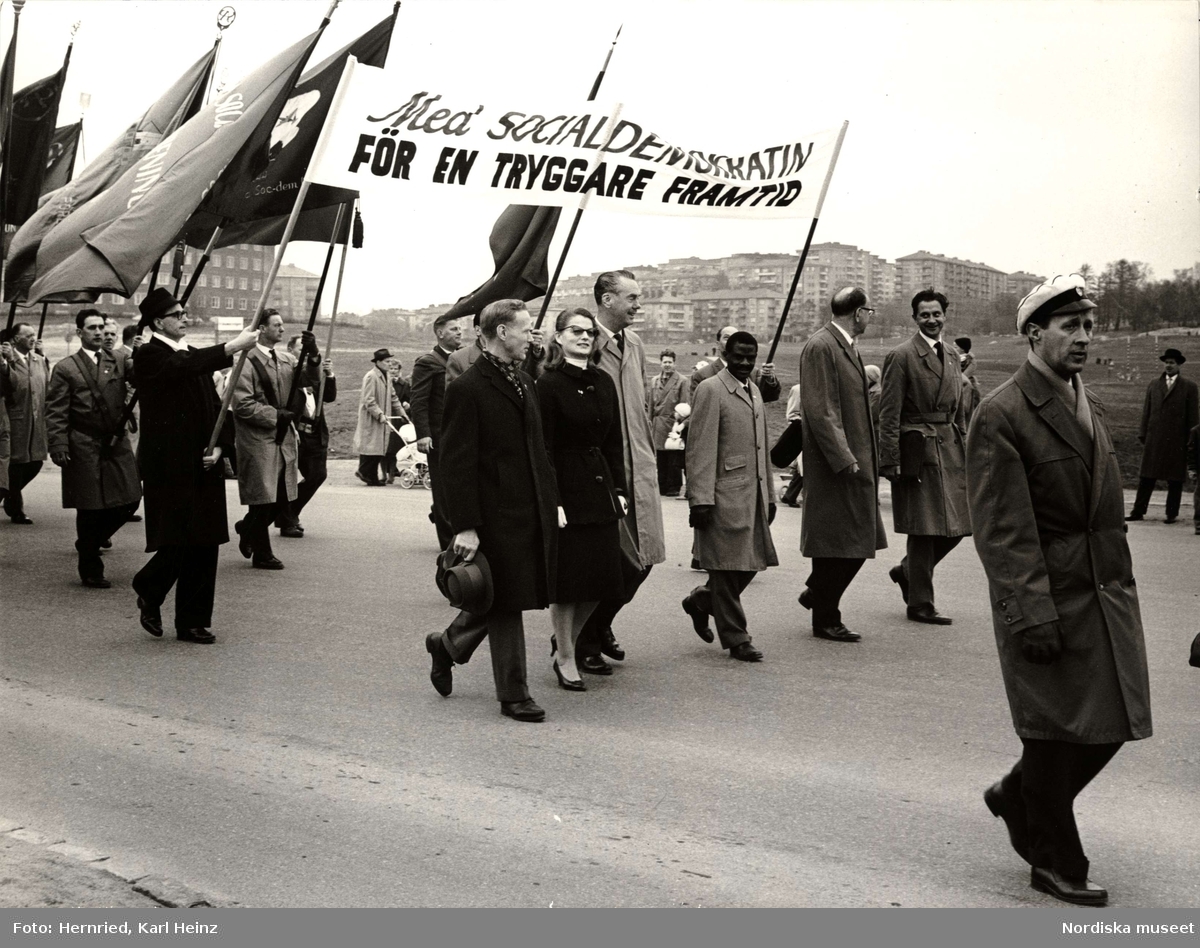 Demonstration 1:a maj. Plakat med texten "Med SOCIALDEMOKRATIN FÖR EN TRYGGARE FRAMTID". Framför plakatet går bland andra Tage Erlander, Sten Andersson, Artur Lundkvist och Maria Wine