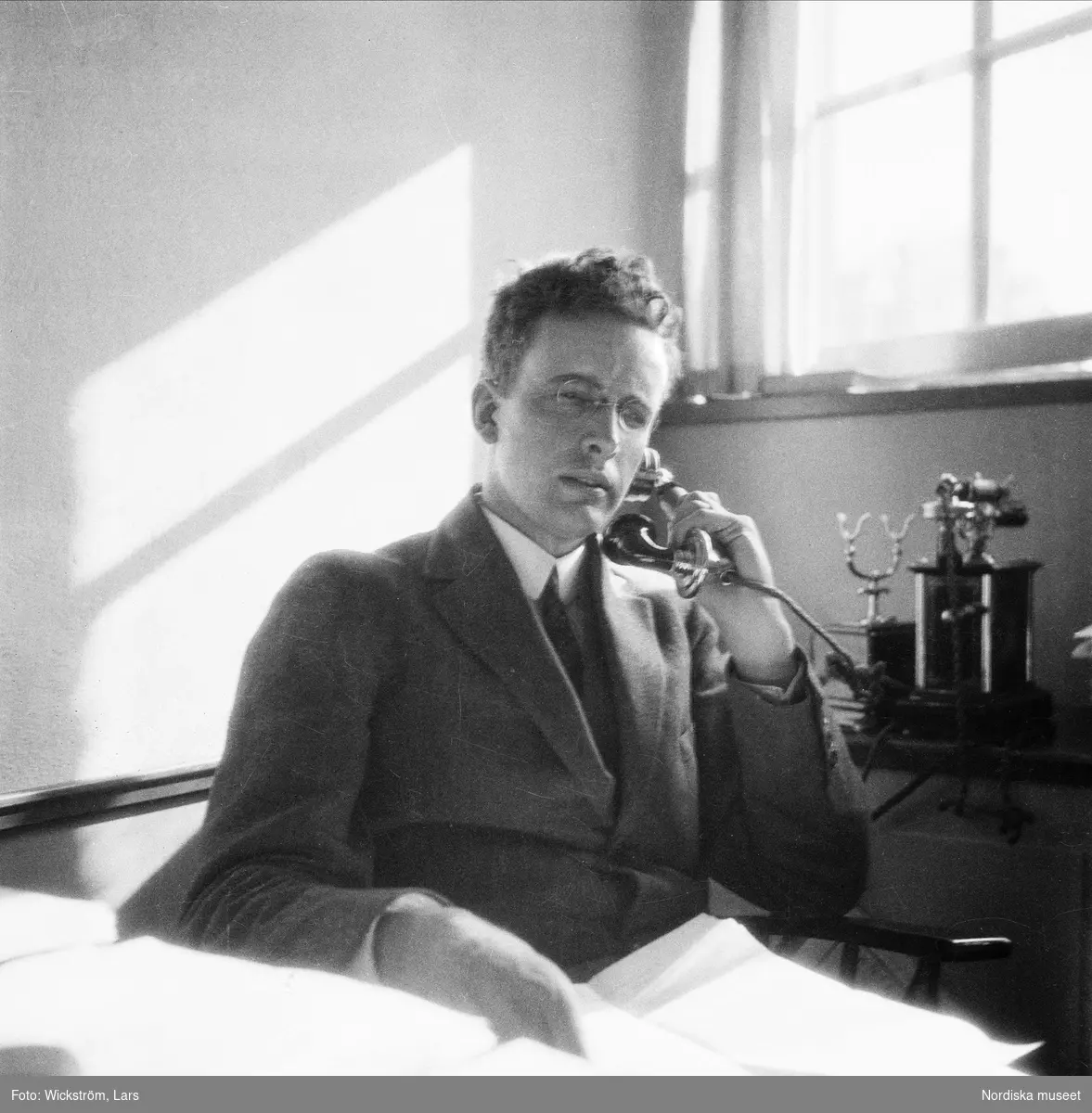 Museimannen Gösta Berg sitter på sitt arbetsrum på Nordiska museet och talar i telefon.