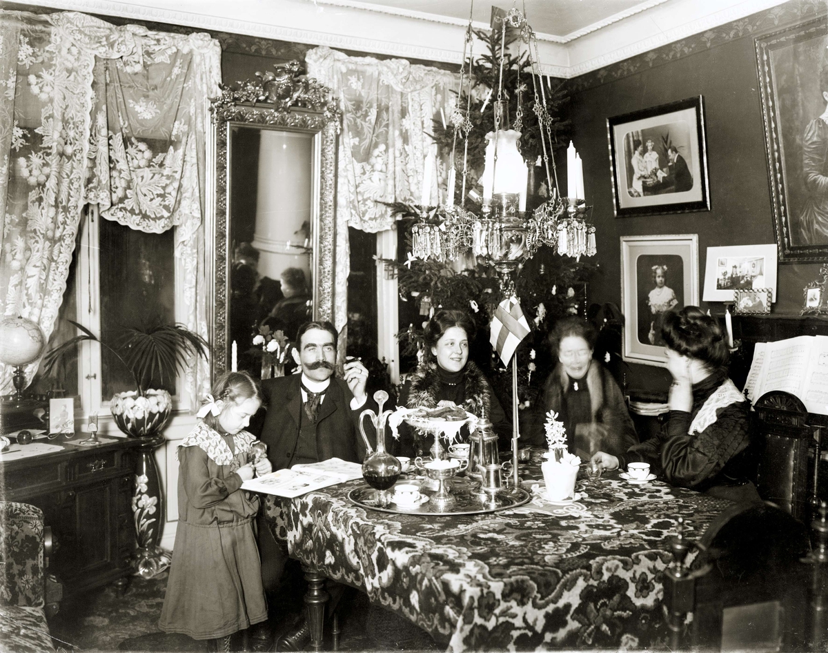 Julfirande, borgerlig hemmiljö runt sekelskiftet 1900. Familj dricker kaffe i salongen. Unionsflagga i miniatyr på bordet.