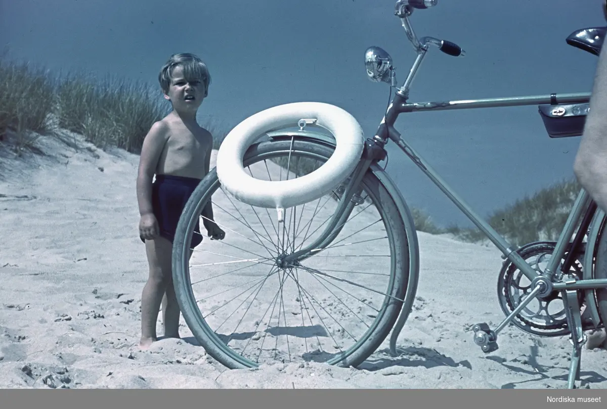Pojke och badring bredvid en cykel. Sandstrand.