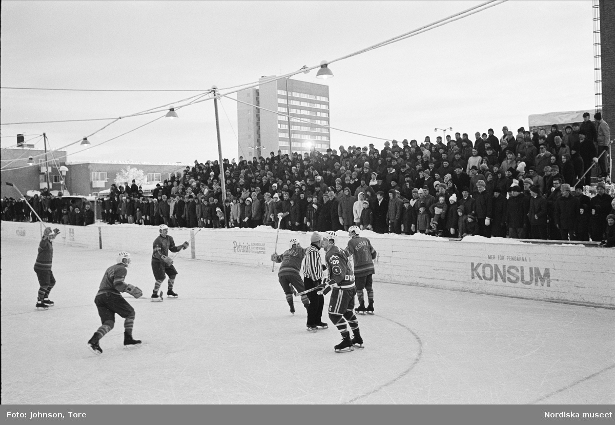 Ishockeymatch i Malmberget. Ishockeyspelare och publik på läktaren vid utomshusrink. 