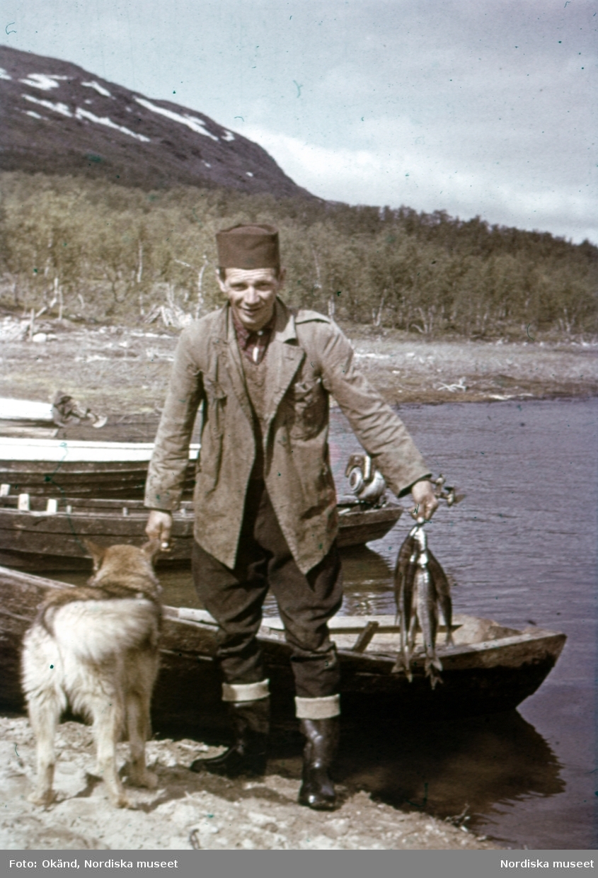 Paulus Utsi stiger i land från roddbåt efter att ha fiskat, hunden står intill. Jokkmokk, 17 juli 1948.