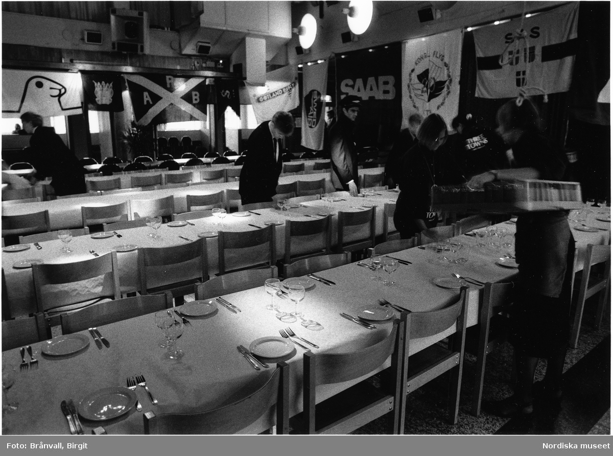 "Phösning", "nollning", för studenter till Flygsektionen vid Kungliga Tekniska högskolan i Stockholm 1993. Serveringspersonla vid bar, dukade bord för festmåltid. Scenframträdande.