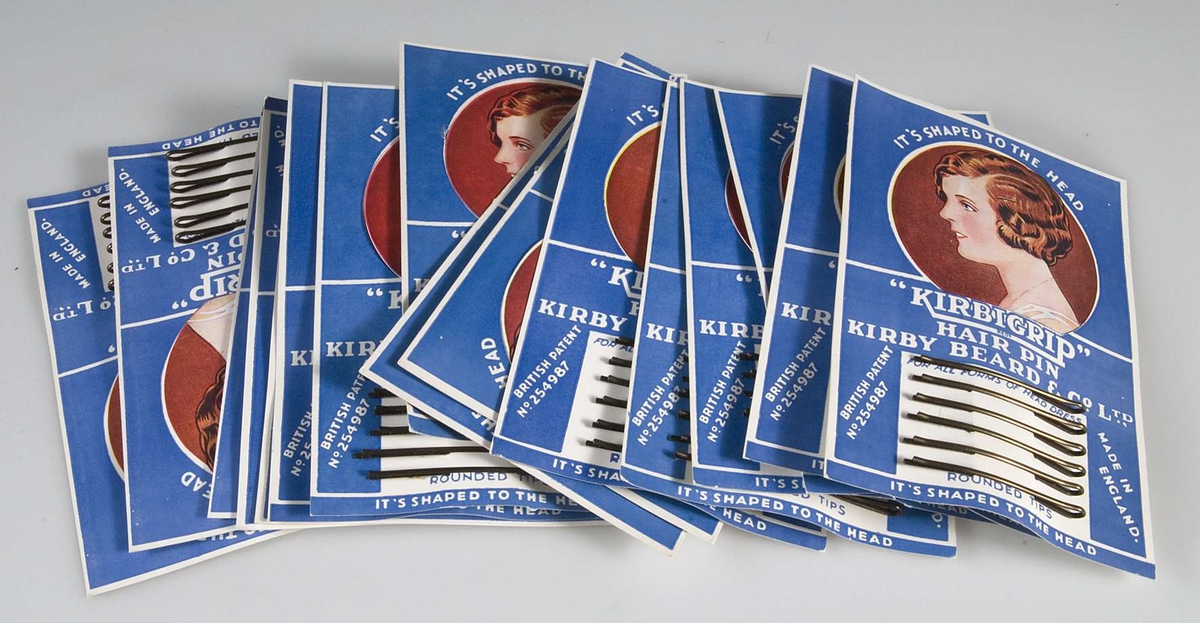 16 förpackningar med sex smala hårspännen i metall. Förpackningen består av blått papper med text i vitt och kvinnoansikte. Text: "KIRBIGRIP" HAIR PIN.

