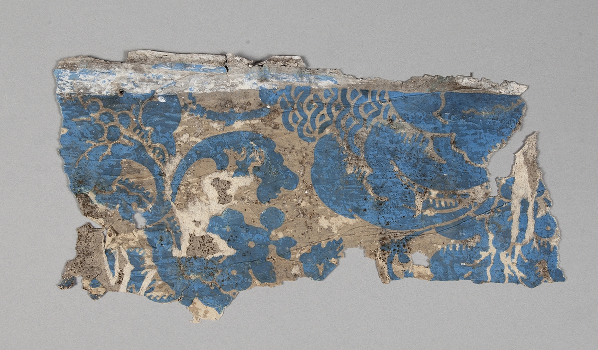 Tapetprovet består av 15 st. fragment. Grundfärgen är beige, med schablonmönster i blått. 