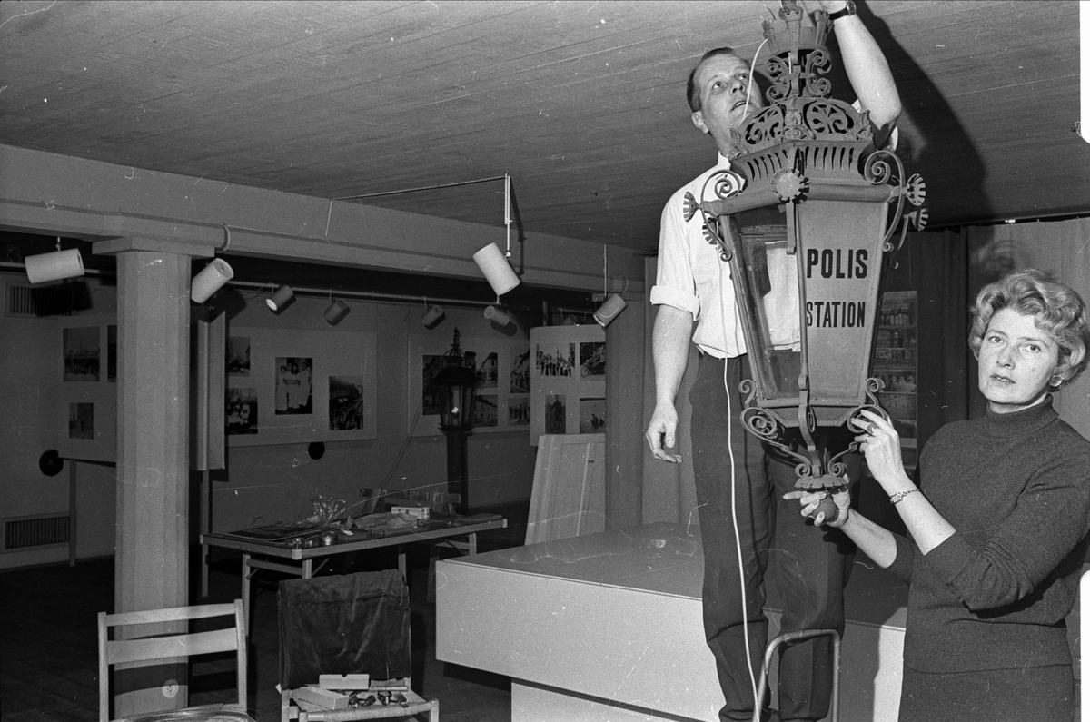 Rustmästare Åke Gustavsson och antikvarie Anna-Märta Berg hänger upp en lykta i utställningen Kameran knäppte, 1890 - 1930, på Upplandsmuseet, Uppsala 1966