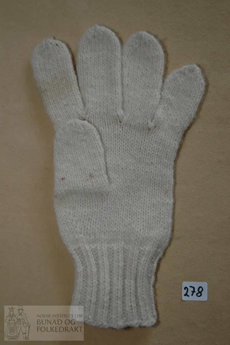 Fingervott strikka i  ubleika, 3-tråds ullgarn. 13 masker pr.5 cm. Vrangbord av 2 vridd rett, 2 vrange før rettstrikk. Plattsaum/snorsting ("løyesaum") med sepyr-garn på handbaken. Nyare type.